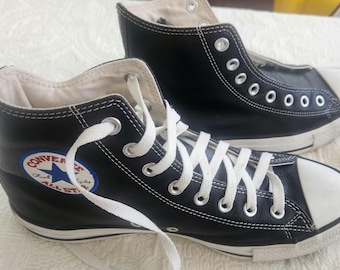 May include: Pair of black high-top sneakers with white laces and a white rubber toe cap. The sneakers feature the Converse All Star logo on the side. The shoes are made of a durable material and are suitable for casual wear.