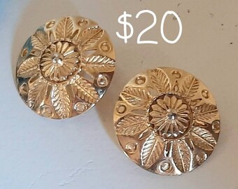 May include: A pair of gold-tone earrings with a floral design. The earrings are round and have a raised design of leaves and flowers. The earrings are £16.