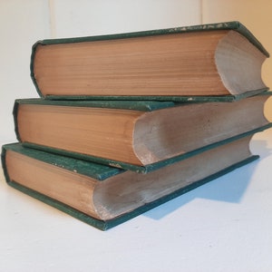 May include: A stack of three hardcover books with green covers and brown spines. The books are arranged in a pyramid shape.