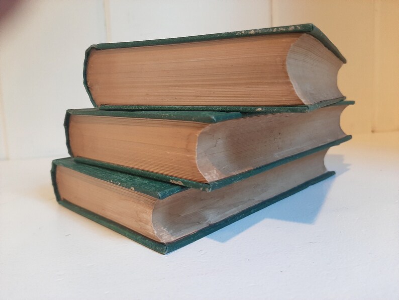 May include: A stack of three hardcover books with green covers and brown spines. The books are arranged in a pyramid shape.