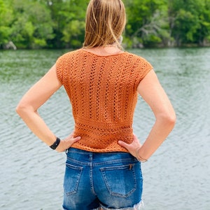 May include: A crocheted top with a sleeveless design in a burnt orange color. The top has a V-neck and a loose fit.