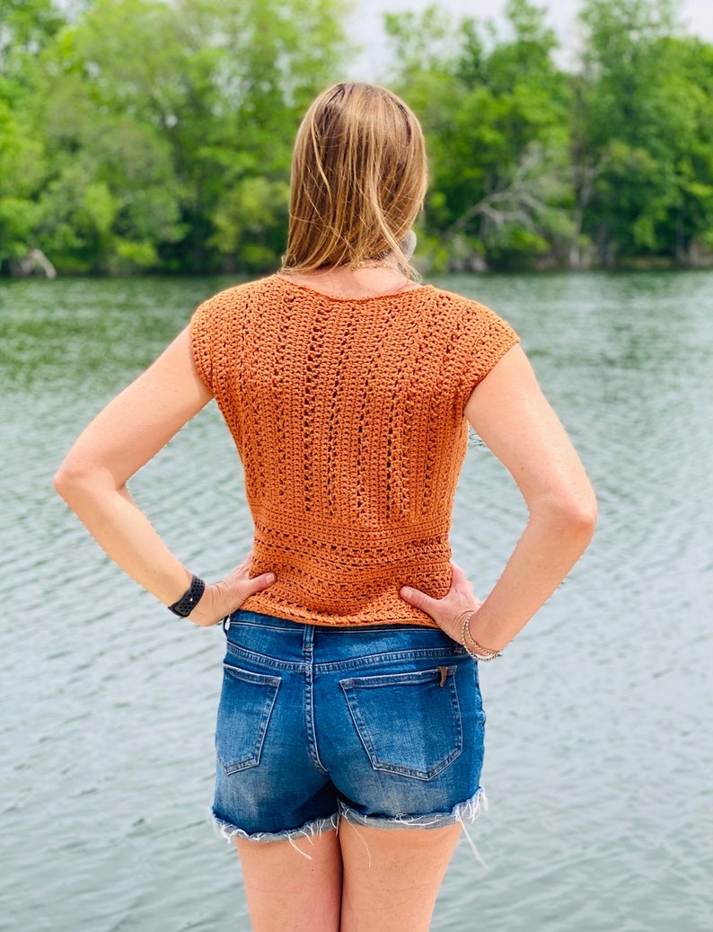 May include: A crocheted top with a sleeveless design in a burnt orange color. The top has a V-neck and a loose fit.