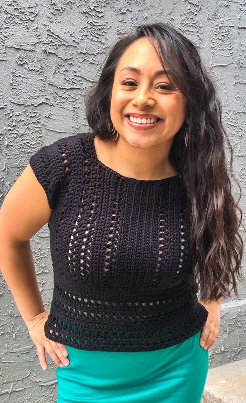 May include: A black crochet top with a delicate openwork pattern. The top has short sleeves and a round neckline. The model is wearing a bright green skirt.