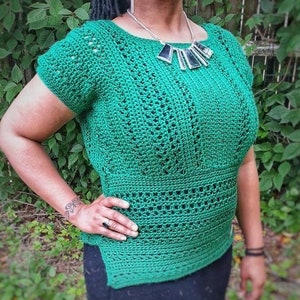 May include: A green crochet top with a wide neckline and short sleeves. The top has a geometric pattern and is worn over a black skirt.