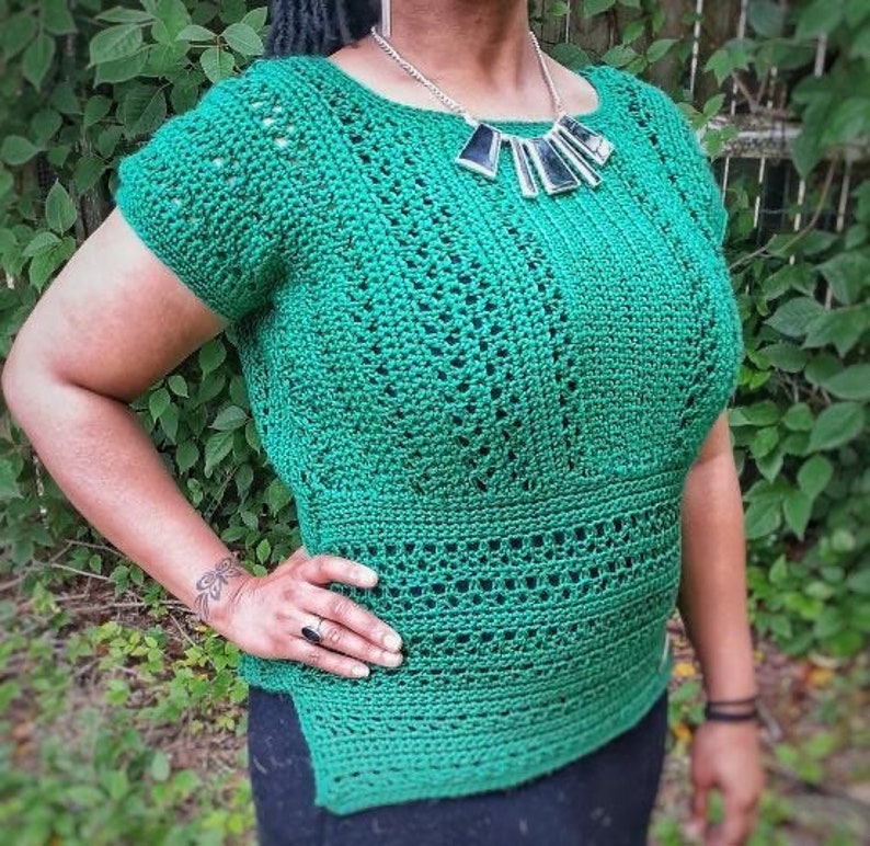 May include: A green crochet top with a wide neckline and short sleeves. The top has a geometric pattern and is worn over a black skirt.