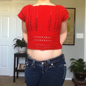 May include: A red crocheted crop top with a lacy design. The top has short sleeves and a square neckline.