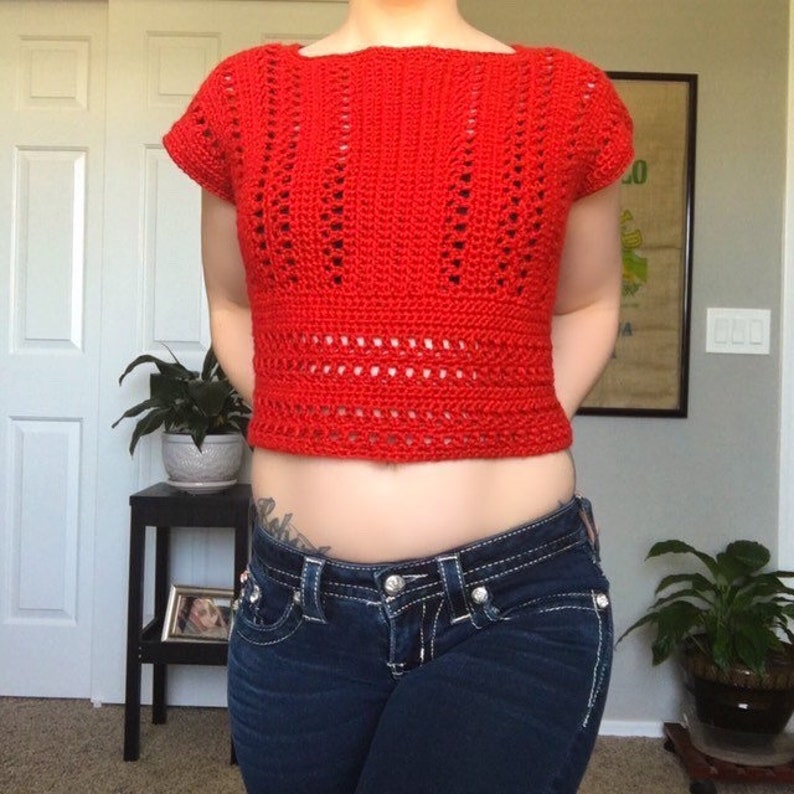 May include: A red crocheted crop top with a lacy design. The top has short sleeves and a square neckline.