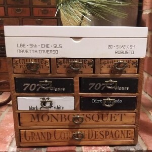 May include: A wooden box with six drawers, each with a different label. The top drawer has a white label with the text "LBE - Shh - EHE - SLS NAVETTA INVERSO" and "20 - 5 1/2 X 54 ROBUSTO". The other drawers have labels with the text "707 Cigare", "Dirtedo", "black white", "MONBOSQUET", and "GRAND CORE DESPAGNE".