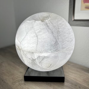 May include: A white alabaster sphere lamp with a black base. The lamp is lit and casts a soft glow.