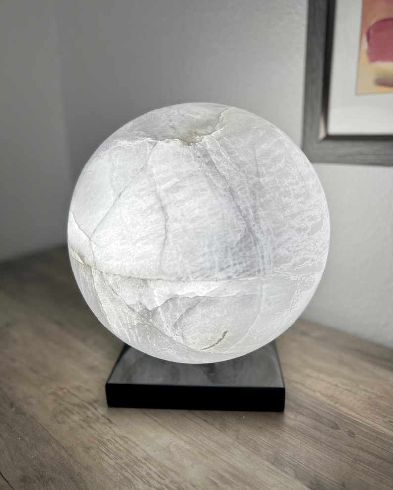 May include: A white alabaster sphere lamp with a black base. The lamp is lit and casts a soft glow.