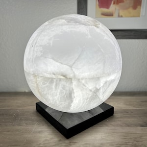May include: A white alabaster sphere lamp with a black square base. The lamp has a natural, veined texture.