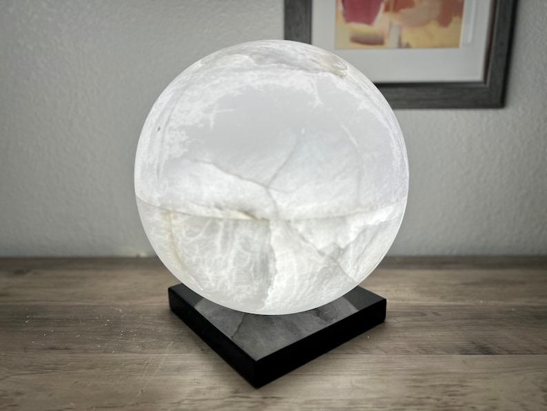 May include: A white alabaster sphere lamp with a black square base. The lamp has a natural, veined texture.