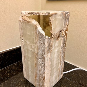 May include: A white and brown onyx lamp base with a unique, natural, and irregular shape. The lamp base is lit from within, creating a warm glow.