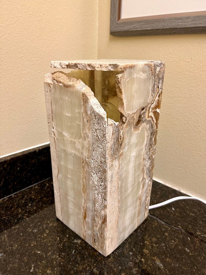 May include: A white and brown onyx lamp base with a unique, natural, and irregular shape. The lamp base is lit from within, creating a warm glow.