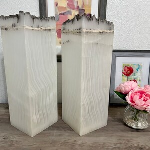 May include: Two white, tall, rectangular vases with a textured, wood-like surface. The vases have a dark gray, uneven top edge.