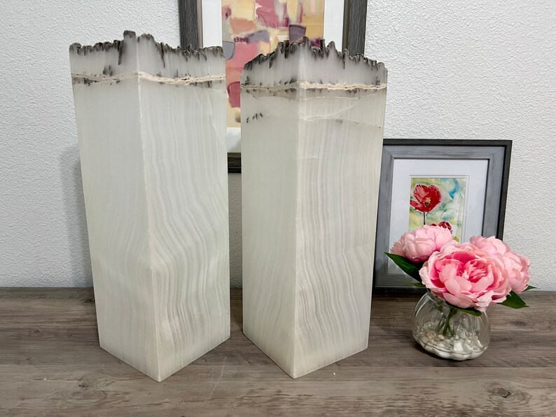May include: Two white, tall, rectangular vases with a textured, wood-like surface. The vases have a dark gray, uneven top edge.