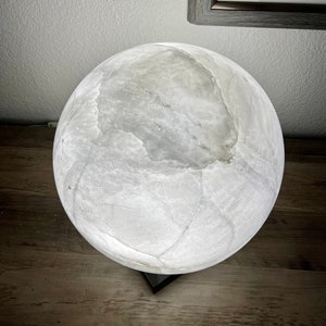 May include: A white alabaster sphere lamp with a black base. The lamp is lit and casts a soft glow.