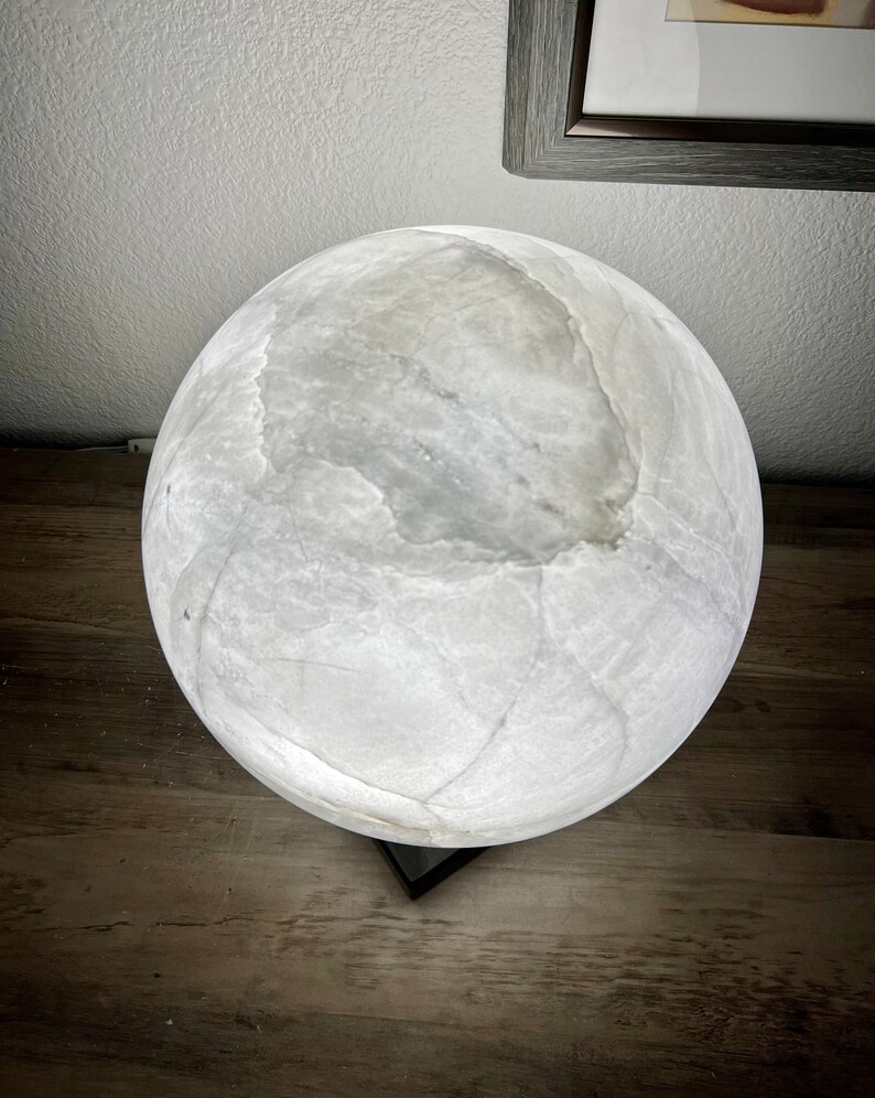 May include: A white alabaster sphere lamp with a black base. The lamp is lit and casts a soft glow.