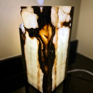 May include: A white onyx lamp with black and brown veins. The lamp is lit and the light shines through the onyx, creating a warm glow.