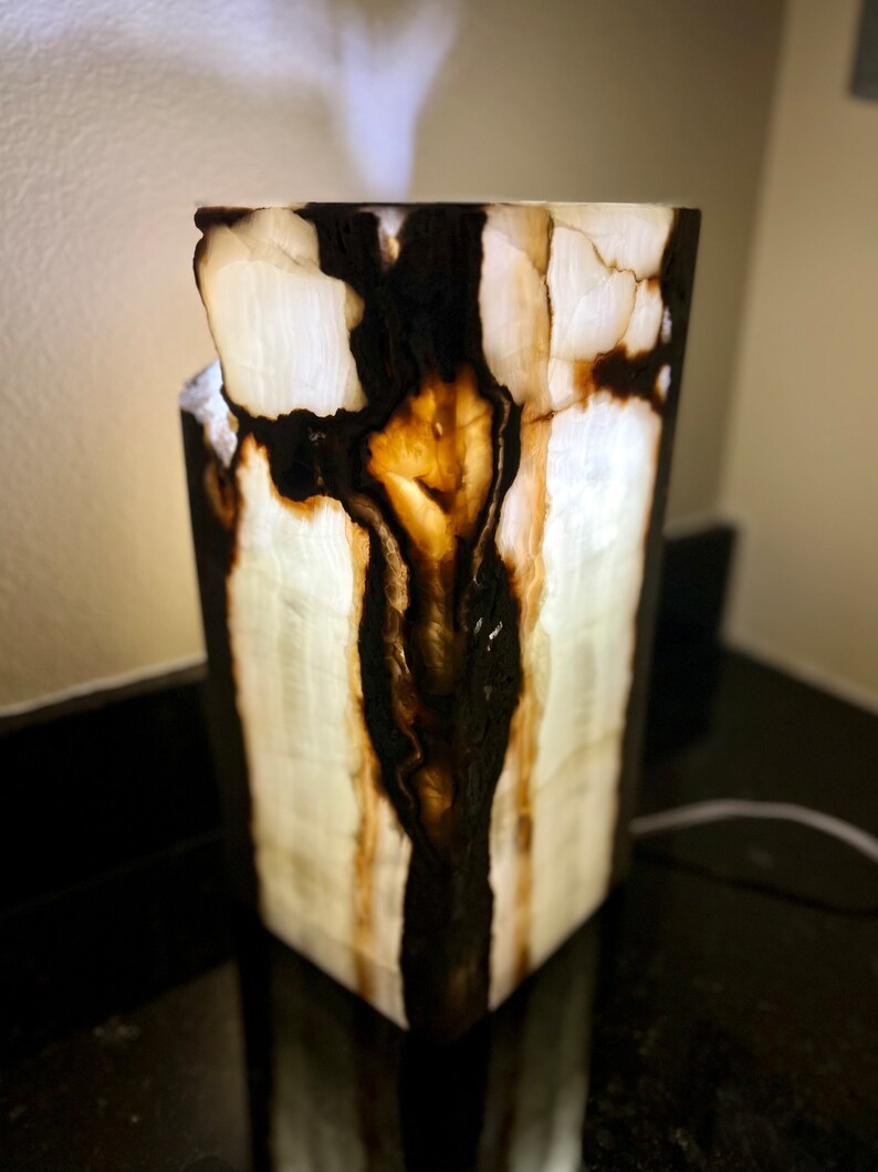 May include: A white onyx lamp with black and brown veins. The lamp is lit and the light shines through the onyx, creating a warm glow.