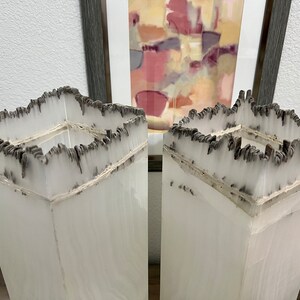 May include: Two tall, white, square vases with a unique, textured, black and white design. The vases are made of a material that resembles paper or parchment.