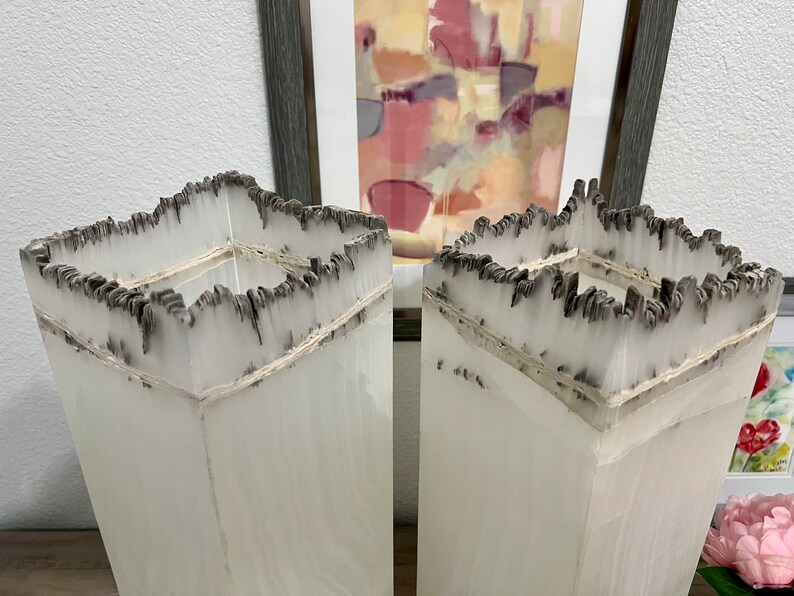 May include: Two tall, white, square vases with a unique, textured, black and white design. The vases are made of a material that resembles paper or parchment.
