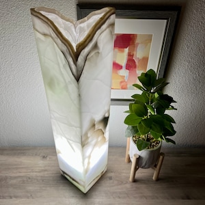 May include: A white and brown onyx lamp with a geometric shape. The lamp is lit and casts a warm glow. The lamp is on a wooden surface.