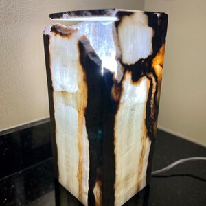 May include: A white onyx lamp with black and brown markings. The lamp is lit and the light shines through the onyx.