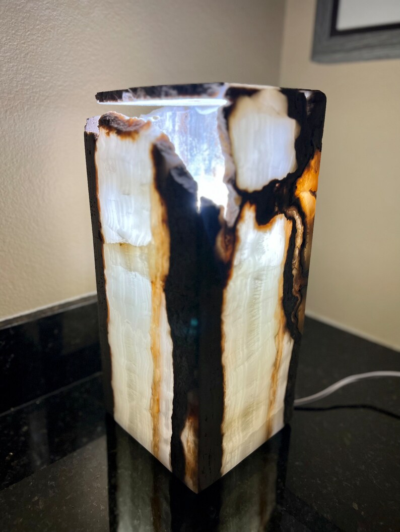 May include: A white onyx lamp with black and brown markings. The lamp is lit and the light shines through the onyx.