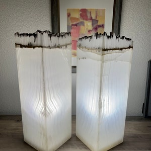 May include: Two white alabaster lamps with a black and white striped pattern. The lamps are lit and casting a warm glow.