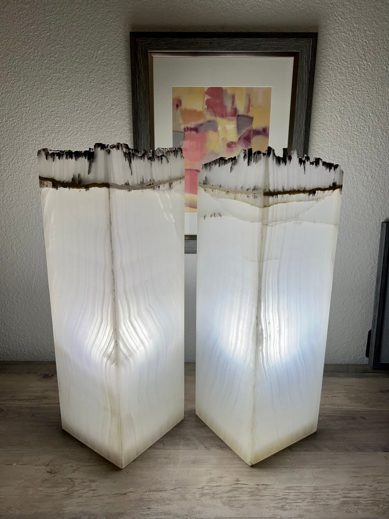 May include: Two white alabaster lamps with a black and white striped pattern. The lamps are lit and casting a warm glow.