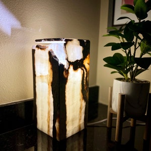 May include: A white and brown onyx lamp with a square base and a light shining through the stone.