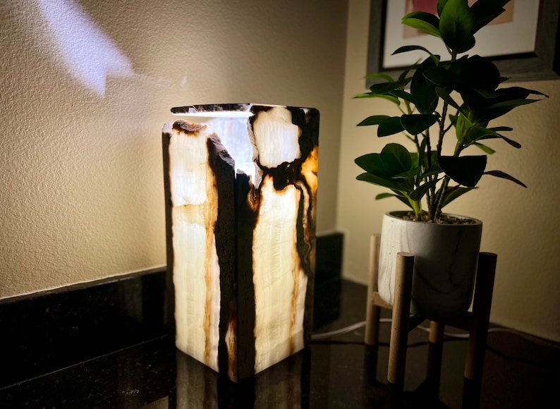 May include: A white and brown onyx lamp with a square base and a light shining through the stone.