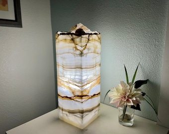 May include: A white and brown onyx lamp with a geometric shape. The lamp is lit and casts a warm glow.