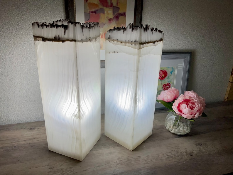 May include: Two white, rectangular lamps with a wood grain pattern and a black top. The lamps are lit and casting a warm glow.
