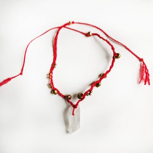 May include: A red string bracelet with gold beads and a clear quartz pendant.