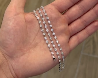 May include: A silver chain necklace with small round clear stones. The necklace is layered on a hand.