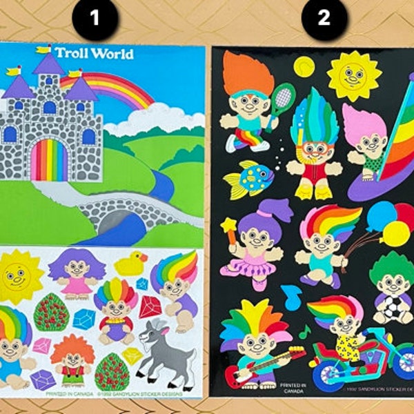 Può includere: Due fogli di carta adesiva con un castello arcobaleno e una varietà di adesivi di troll. Il primo foglio ha un castello con un arcobaleno e un ponte. Il secondo foglio ha una varietà di troll con diversi stili di capelli, vestiti e accessori. Il testo "Troll World" è stampato sul primo foglio.