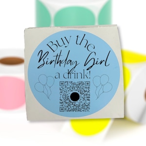 May include: A blue and white round sticker with the text "Buy the Birthday Girl a drink!" and a black and white QR code. The sticker is on a white background.
