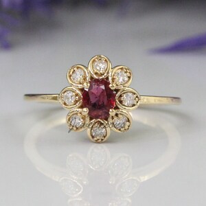 May include: A gold ring with a red gemstone surrounded by smaller white gemstones in a flower shape.