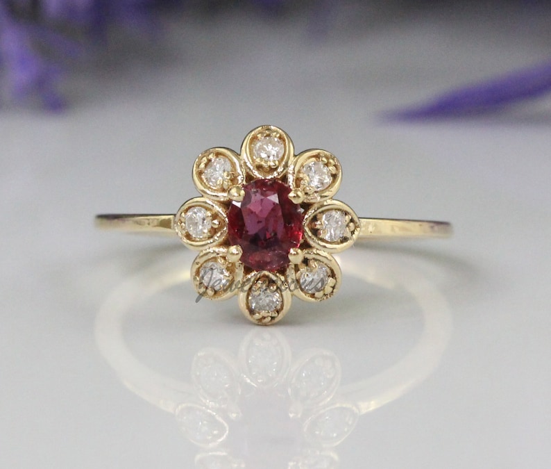 May include: A gold ring with a red gemstone surrounded by smaller white gemstones in a flower shape.