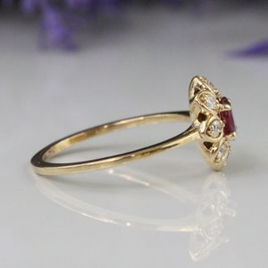 May include: A gold ring with a red gemstone surrounded by smaller white gemstones.
