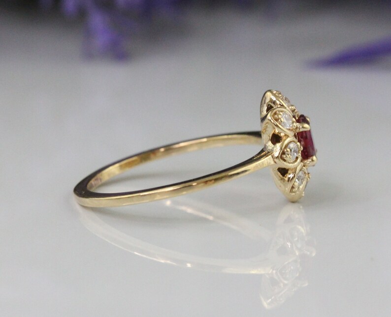 May include: A gold ring with a red gemstone surrounded by smaller white gemstones.