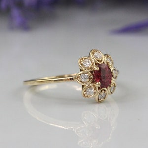 May include: A gold ring with a red gemstone surrounded by smaller white gemstones in a flower-like design.