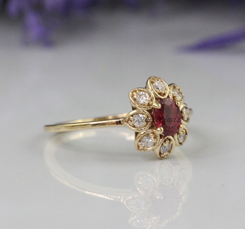 May include: A gold ring with a red gemstone surrounded by smaller white gemstones in a flower-like design.