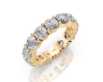 May include: A gold eternity ring featuring a continuous row of round-cut diamonds. The ring has a polished finish and is marked with "14K". The diamonds sparkle, reflecting light. The ring is set against a white background.