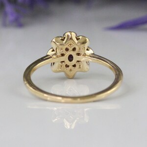 May include: A gold ring with a flower-shaped design featuring a purple gemstone in the center. The ring is set with smaller gemstones around the center stone.