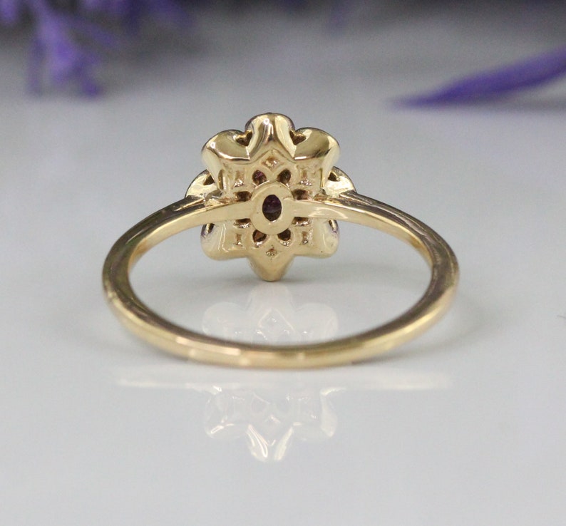 May include: A gold ring with a flower-shaped design featuring a purple gemstone in the center. The ring is set with smaller gemstones around the center stone.