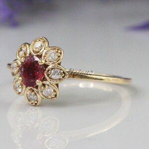 May include: A gold ring with a red gemstone surrounded by smaller white gemstones in a flower shape.