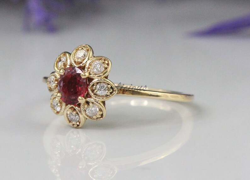 May include: A gold ring with a red gemstone surrounded by smaller white gemstones in a flower shape.